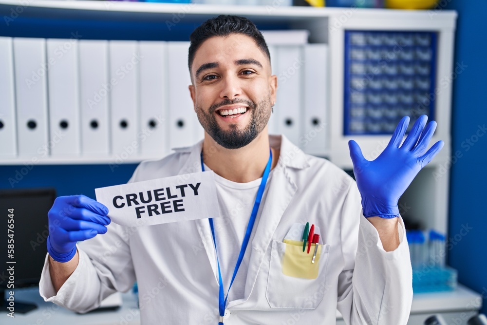 Young handsome man working at scientist laboratory holding cruelty free banner celebrating victory with happy smile and winner expression with raised hands Young handsome man working at scientist laboratory holding cruelty free banner celebrating victory with happy smile and winner expression with raised hands
