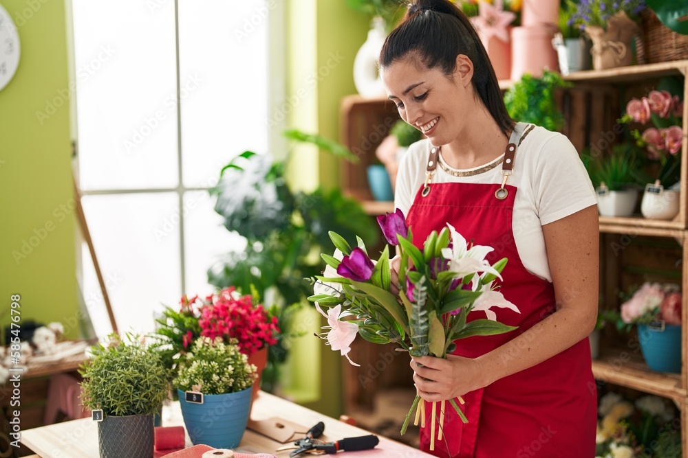 Young beautiful hispanic woman florist holding bouquet of flowers at flower shop