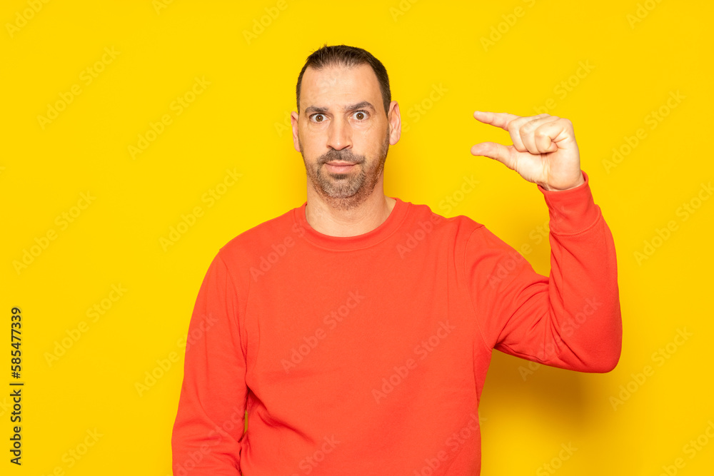 Handsome hispanic man with beard a red sweater gesturing with his hand making a small size sign with fingers looking and camera. Measurement concept. Isolated on yellow background Handsome hispanic man with beard a red sweater gesturing with his hand making a small size sign with fingers looking and camera. Measurement concept. Isolated on yellow background