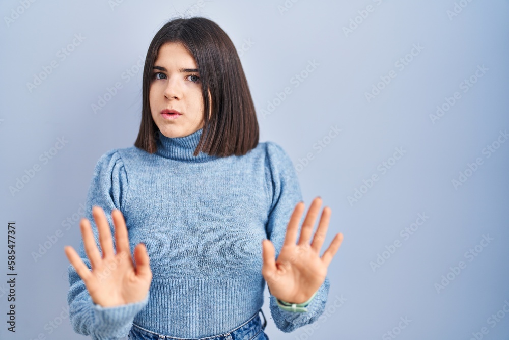 Young hispanic woman standing over blue background moving away hands palms showing refusal and denial with afraid and disgusting expression. stop and forbidden. Young hispanic woman standing over blue background moving away hands palms showing refusal and denial with afraid and disgusting expression. stop and forbidden.