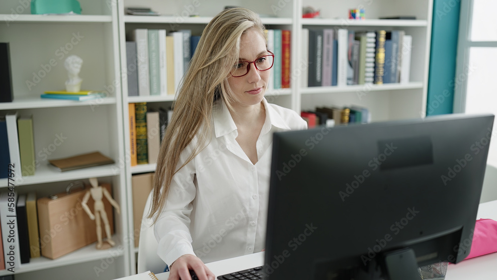 Young blonde woman student using computer sitting on table at library university Young blonde woman student using computer sitting on table at library university