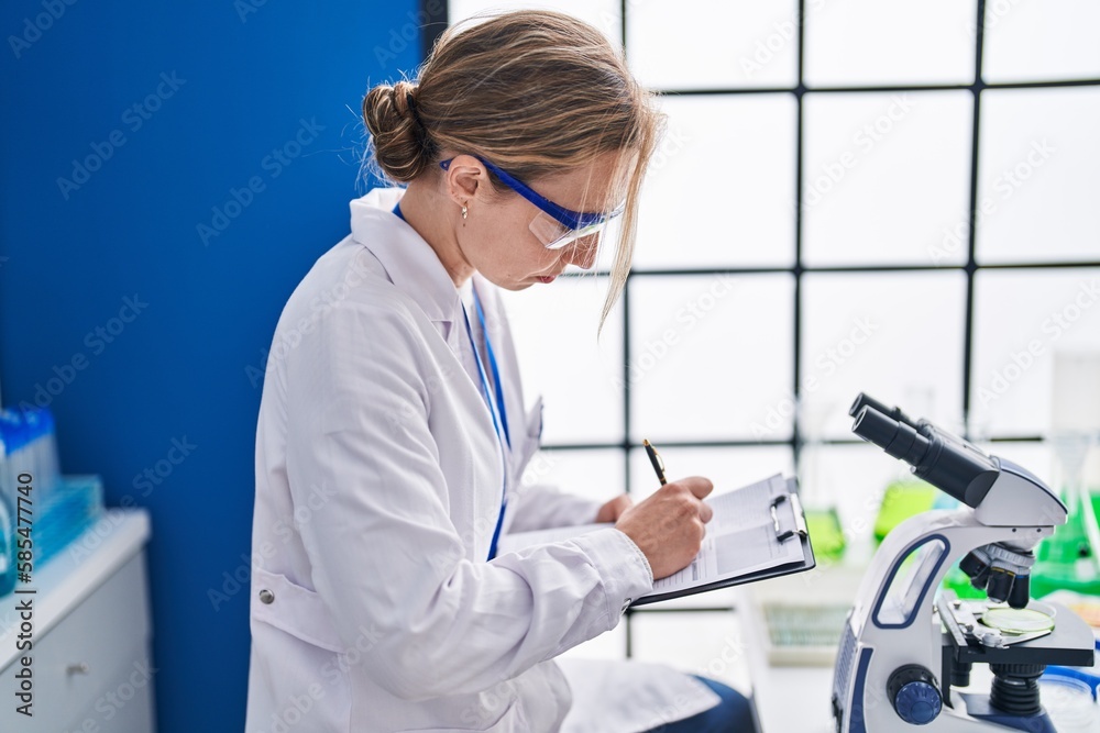 Young blonde woman scientist writing report working at laboratory Young blonde woman scientist writing report working at laboratory