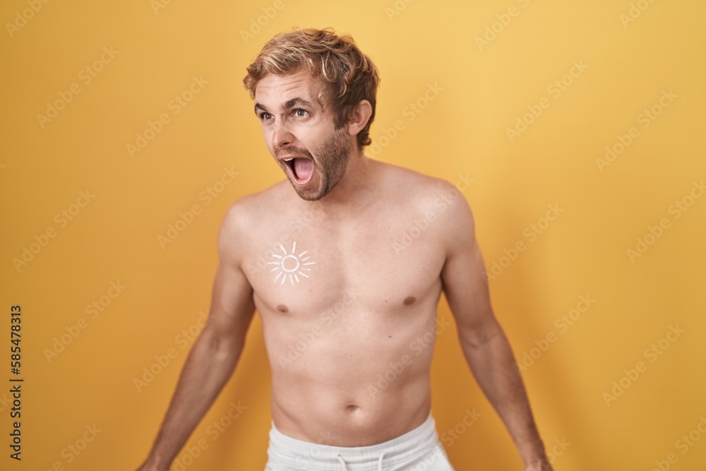Caucasian man standing shirtless wearing sun screen angry and mad screaming frustrated and furious, shouting with anger. rage and aggressive concept.