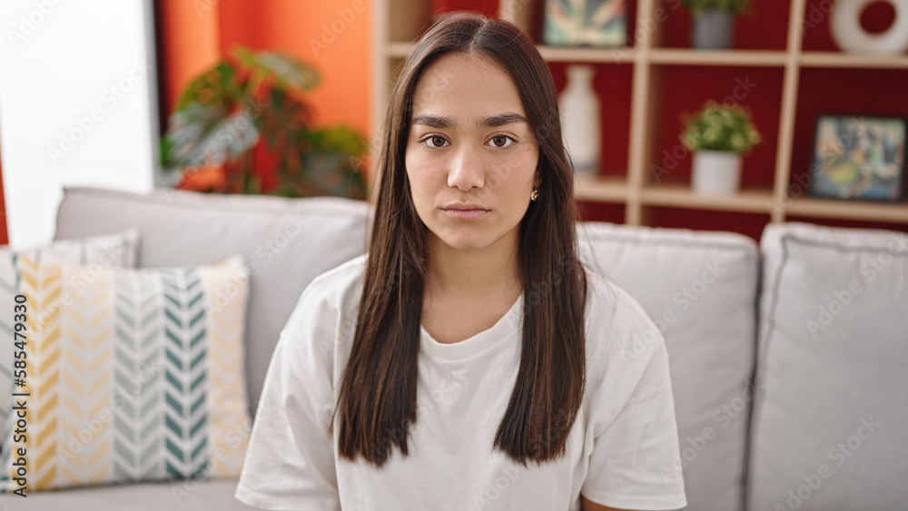 Young beautiful hispanic woman sitting on sofa with serious expression at home Young beautiful hispanic woman sitting on sofa with serious expression at home