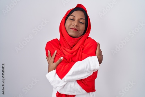 Young arab woman wearing traditional islamic hijab scarf hugging oneself happy and positive, smiling confident. self love and self care