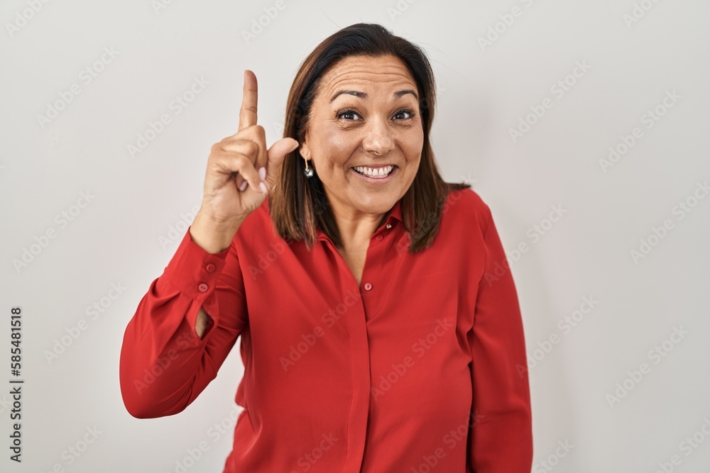 Hispanic mature woman standing over white background pointing finger up with successful idea. exited and happy. number one. Hispanic mature woman standing over white background pointing finger up with successful idea. exited and happy. number one.