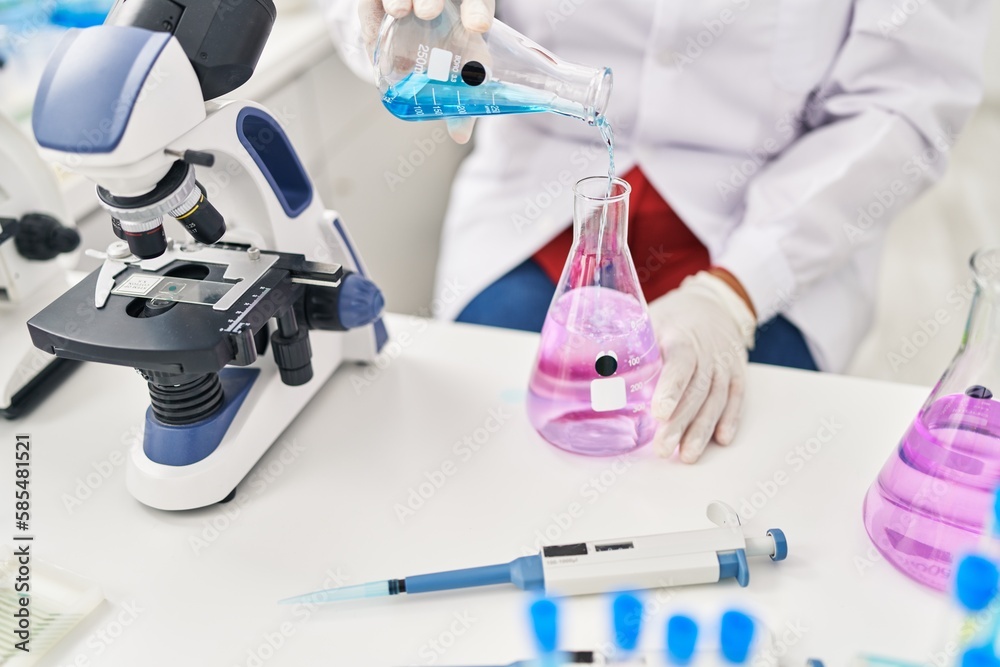Middle age hispanic woman wearing scientist measuring liquid at laboratory Middle age hispanic woman wearing scientist measuring liquid at laboratory