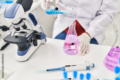 Middle age hispanic woman wearing scientist measuring liquid at laboratory