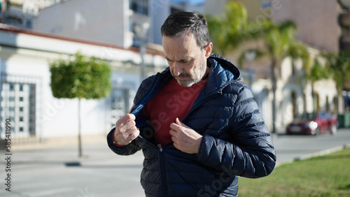 Middle age man standing with serious expression looking for something on jacket at street