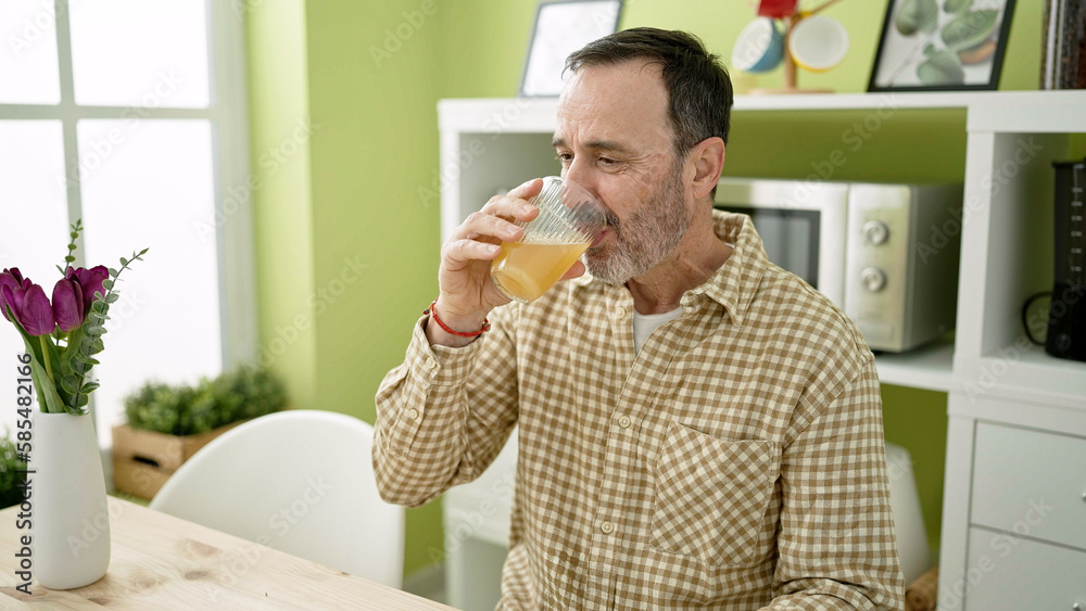 Middle age man drinking orange juice sitting on table at home