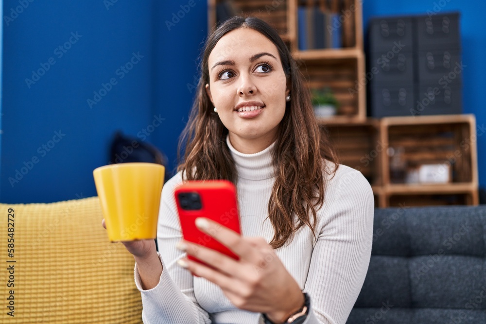 Young beautiful hispanic woman using smartphone drinking coffee at home Young beautiful hispanic woman using smartphone drinking coffee at home