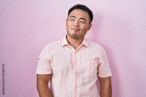 Chinese young man standing over pink background smiling looking to the side and staring away thinking.