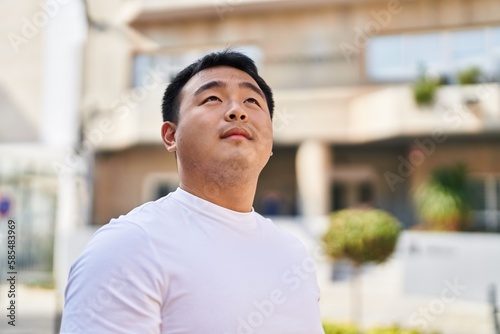 Young chinese man smiling confident looking to the sky at street