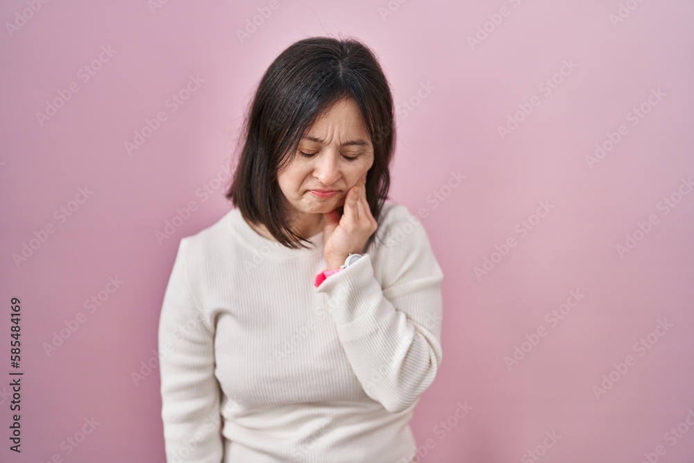 Woman with down syndrome standing over pink background touching mouth with hand with painful expression because of toothache or dental illness on teeth. dentist Woman with down syndrome standing over pink background touching mouth with hand with painful expression because of toothache or dental illness on teeth. dentist