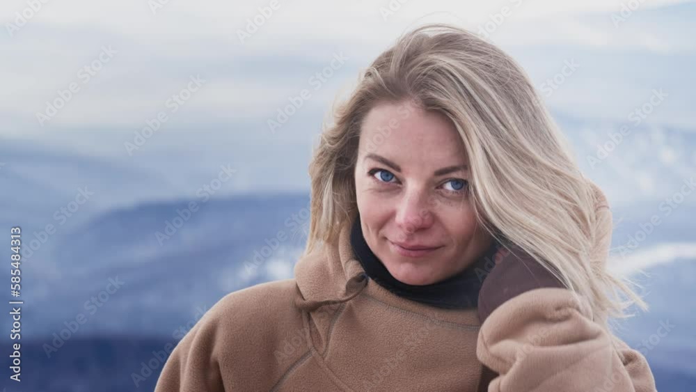 Portrait of a beautiful girl will fix her hair in winter. Beautiful big blue Eyes, Wind blowing on Blonde Hair. Happy skiing. Dressed in a hoodie. Travel to winter resort, adventure. Slow motion Portrait of a beautiful girl will fix her hair in winter. Beautiful big blue Eyes, Wind blowing on Blonde Hair. Happy skiing. Dressed in a hoodie. Travel to winter resort, adventure. Slow motion