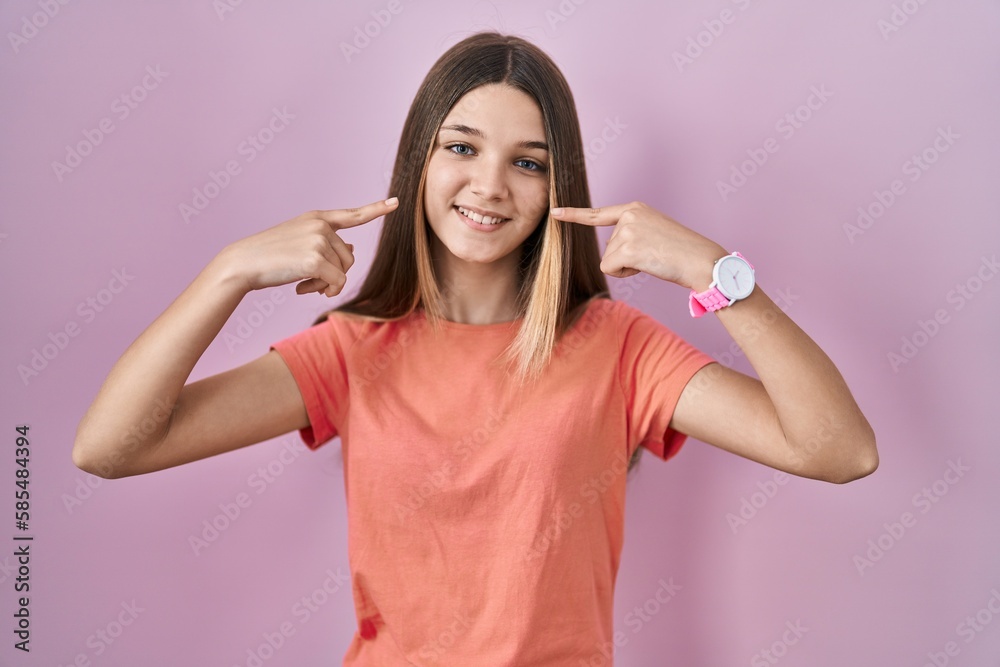 Fototapeta premium Teenager girl standing over pink background smiling cheerful showing and pointing with fingers teeth and mouth. dental health concept.