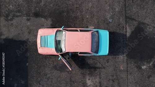 Driver in helmet gets into car with open door. Racing automobile repainted in blue and pink colors stands on asphalt training circuit view from above photo