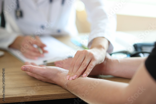 Doctor checkups patient pulse on wrist in medical office