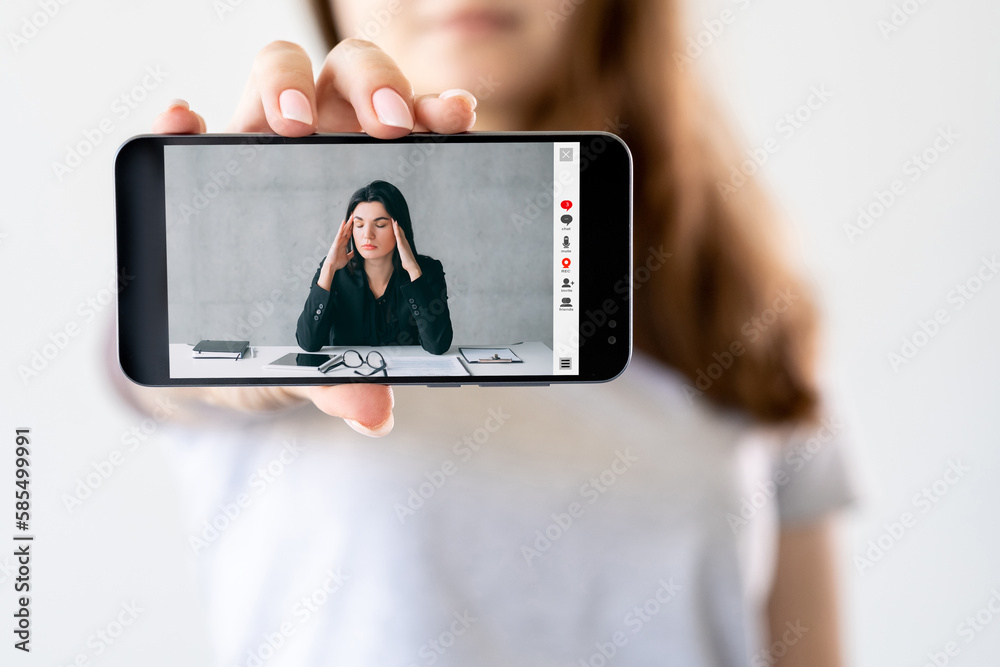 Video conference. Work fatigue. Professional stress. Tired business woman suffering from headache massaging temples online on phone screen in hand on neutral white.