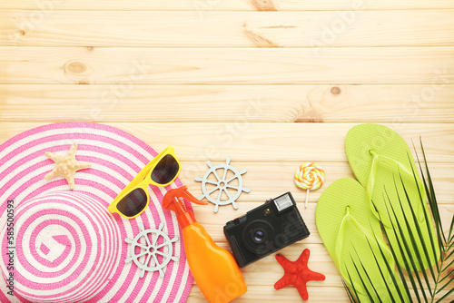 Pink straw hat with flip flops, sunglasses, starfishes and retro camera on brown wooden background
