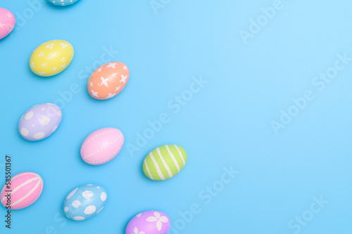 Happy Easter holiday greeting card design concept. Colorful Easter Eggs and spring flowers on blue background. Flat lay  top view  copy space.