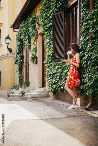 Young beautiful woman in a red dress with a cup on  European street © Олександр Пшевлоцьки
