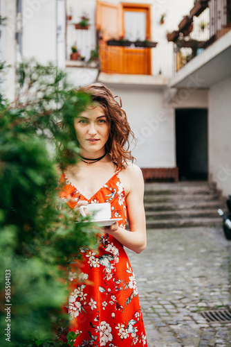 Young beautiful woman in a red dress with a cup on  European street