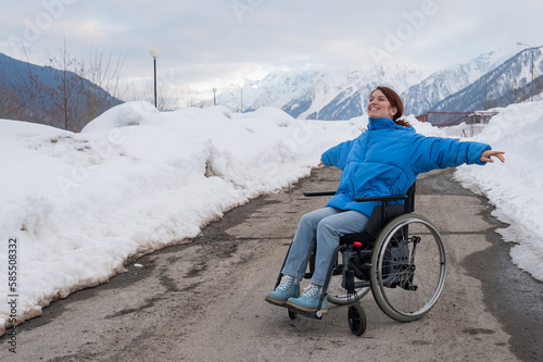 A woman in a wheelchair spread her arms to the side like wings in the mountains in winter.