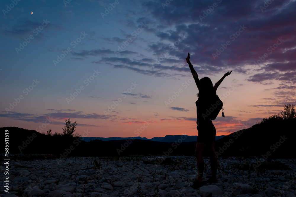 A silhouette of a female traveler standing in the mountains during sunset
