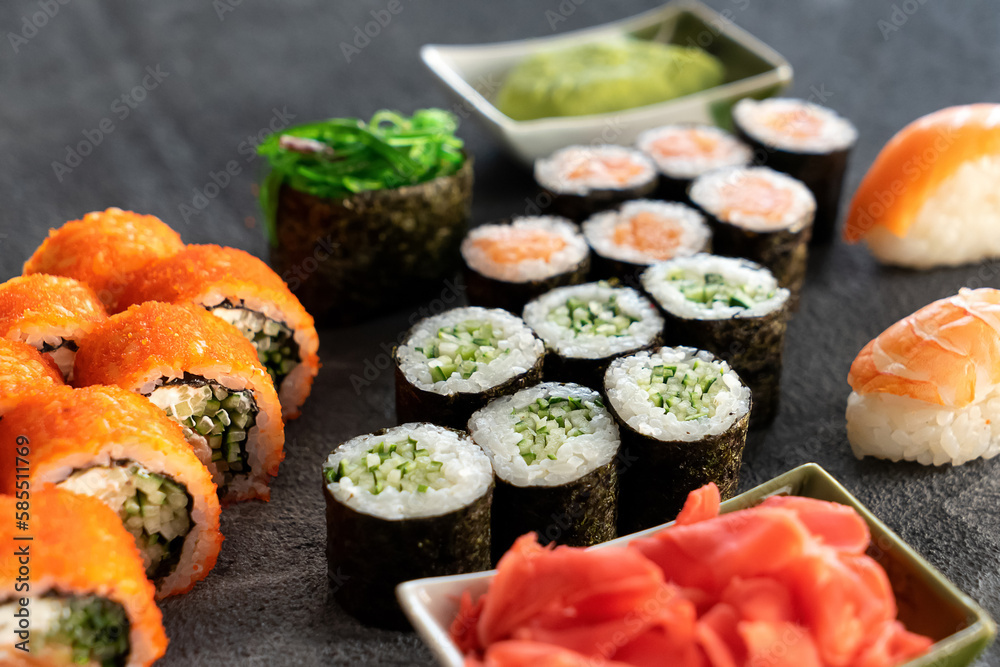 Set of different sushi and sushi rolls with wasabi and ginger. Maki rolls with cucumber, salmon, hiashi. Uramaki with tobiko caviar. Sushi with salmon. Gray background. Side view. 