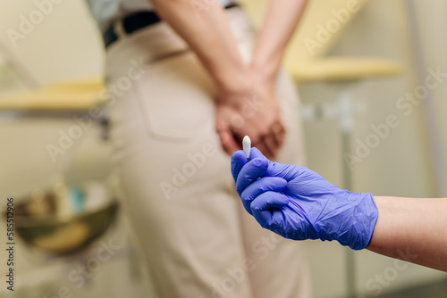 Woman at a proctologist's appointment. The doctor holds a rectal suppository before entering the anus. Hemorrhoids or prostate treatment concept.