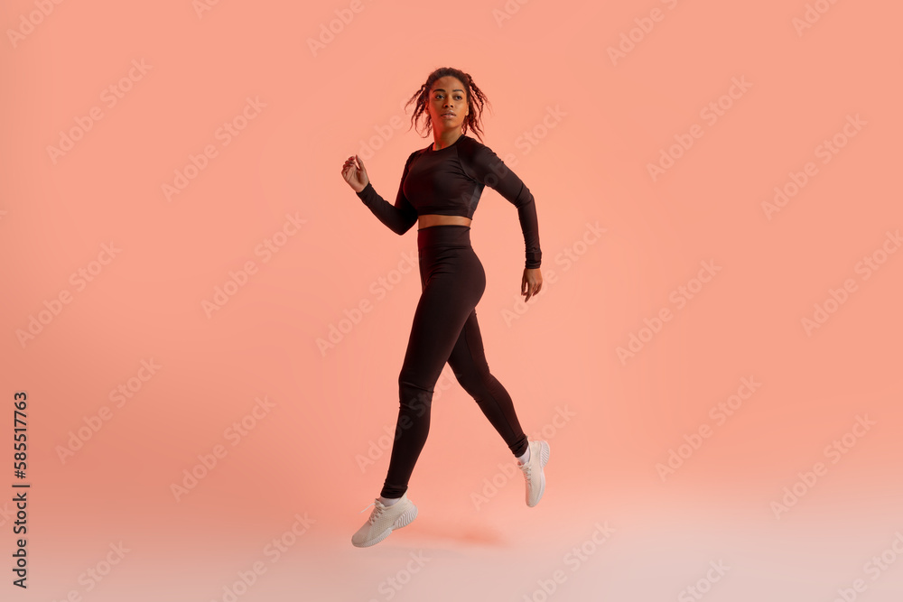 Black female athlete jumping, running, exercising during training over neon studio background, full length