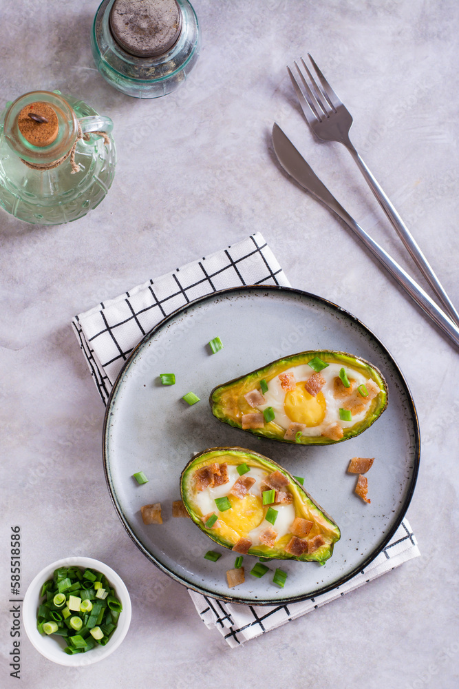 Egg baked in avocado sprinkled with bacon and herbs on a plate top and vertical view