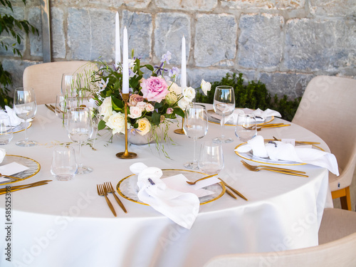 Wedding banquet concept. Chairs and round table for guests, served with cutler and, flowers and crockery and covered with a tablecloth