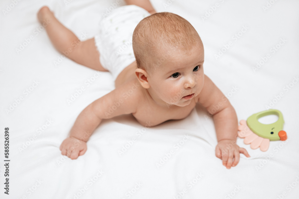 A newborn baby in a diaper is lying on a stomach on a white blanket and playing with a toy. A newborn baby in a diaper is lying on a stomach on a white blanket and playing with a toy.