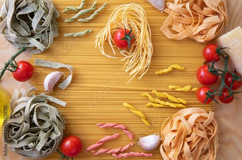 Italian pasta farfalle on the background of spaghetti, fusilli and fettuccine placer on the table, cherry tomatoes, garlic, Italian pasta of different colors photo