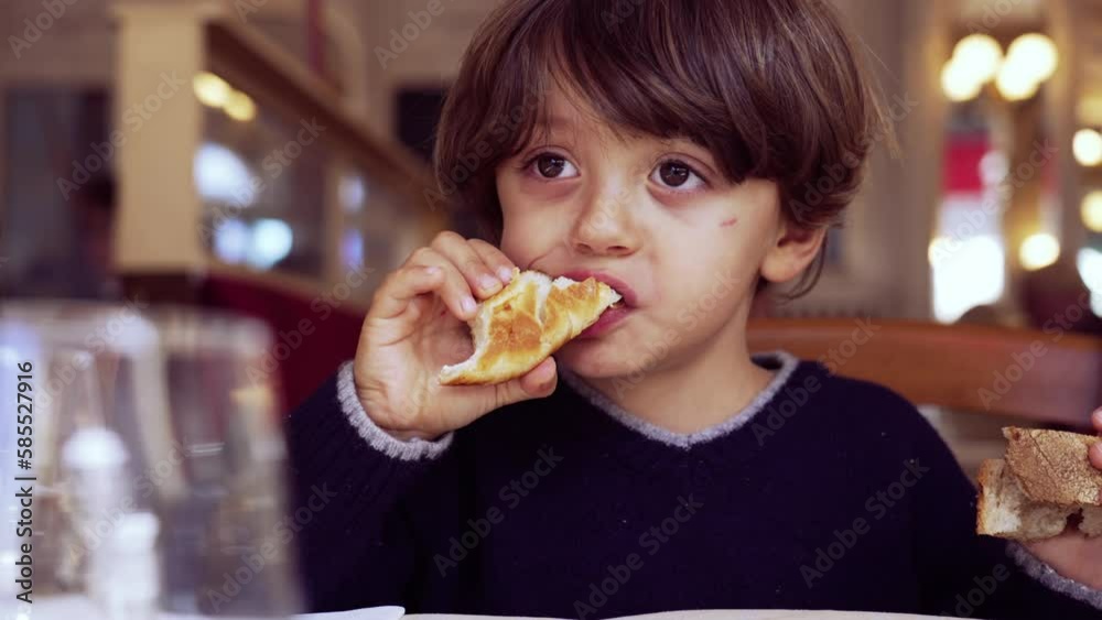 Child eating bread sitting at restaurant. One little boy eats piece of carb food croissant Child eating bread sitting at restaurant. One little boy eats piece of carb food croissant