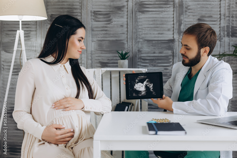 Doctor showing a pregnant girl picture ultrasound. She came to the doctor in the clinic. It's a gynecologist. He is dressed in a white robe Doctor showing a pregnant girl picture ultrasound. She came to the doctor in the clinic. It's a gynecologist. He is dressed in a white robe