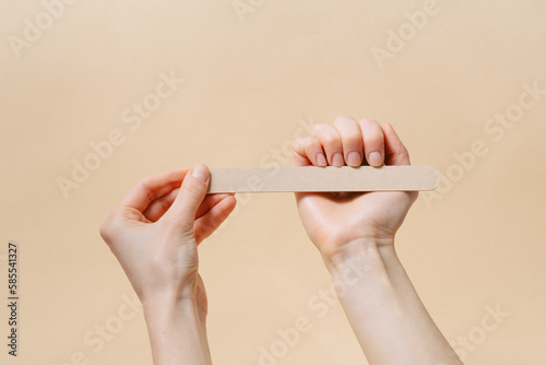 Female fragile hands make a natural manicure by filing nails with a file on a beige isolated background. Self care and beauty salon concept.