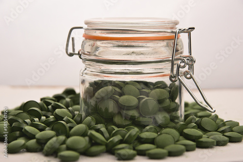 Green tablets of bio chlorella in a glass jar. A health-promoting dietary supplement rich in vitamins. Chlorella vulgaris.