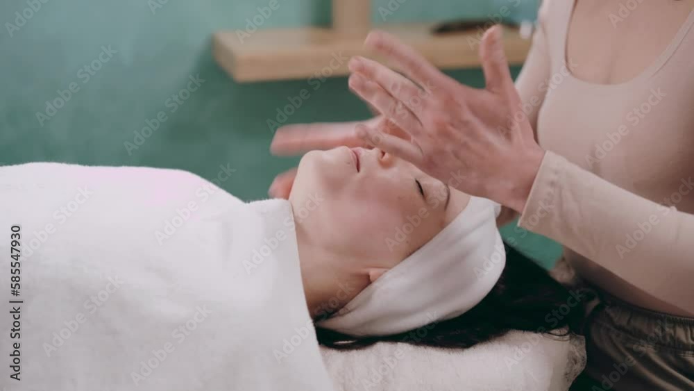 The beautician makes a facial massage. Young woman lies on her back and gets a facelift in a spa salon. Massage techniques for anti-aging.