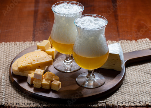 Glasses of Belgian light blonde beer made in abbey and wooden board with variety of belgian cheeses photo