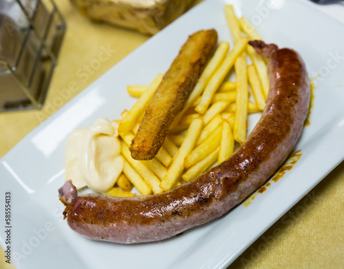 Fried tasty rustic sausage with french fries served at plate with white sauce