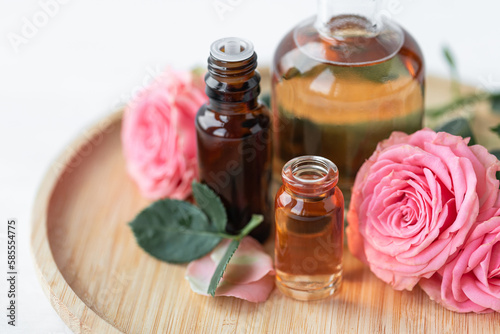 Aromatherapy. Concept of pure organic essential rose oil. Elixir with plant based floral or herbal ingredients. Pink flowers extract. Spa atmosphere with candle, towel. White background