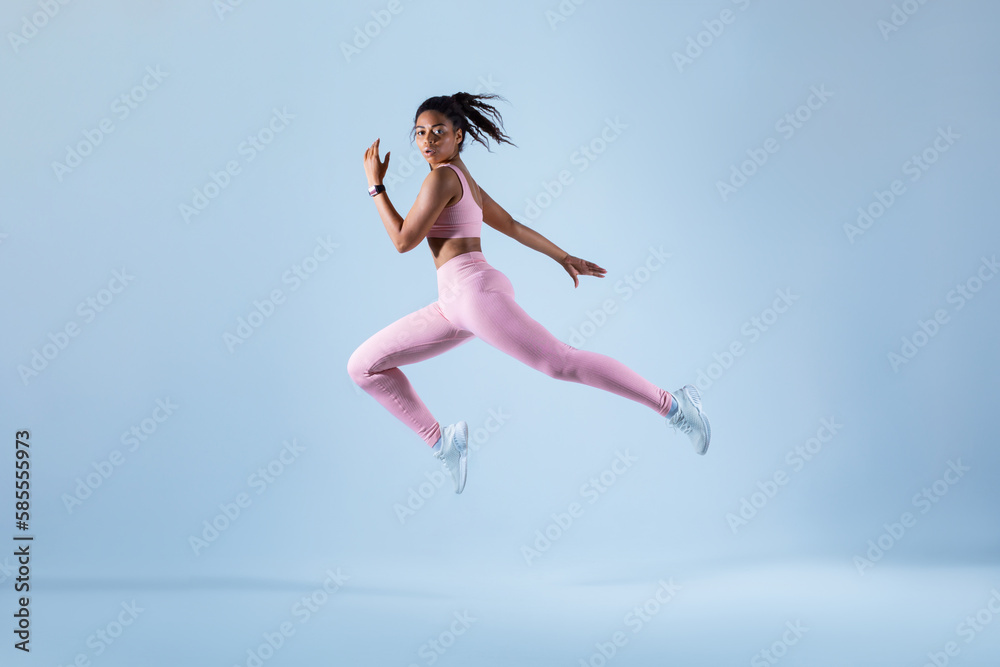 Training concept. Fit black woman in sportswear jumping or running, exercising on neon blue studio background
