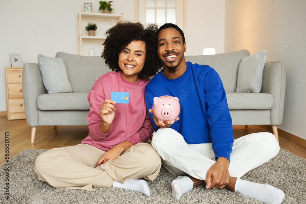 Black Couple Showing Credit Card And Piggybank With Savings Indoors