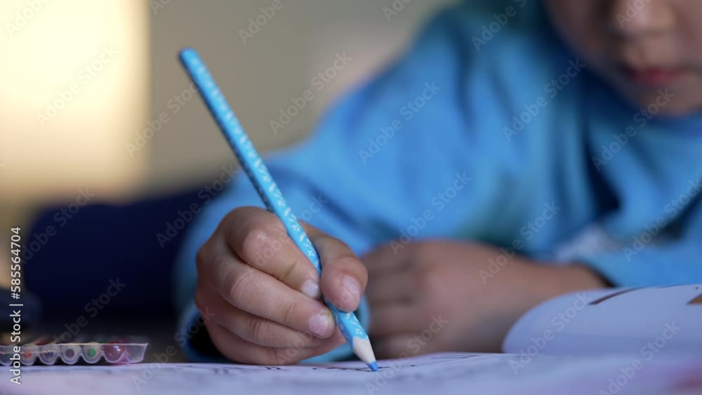Child hand holding color pencil drawing on paper. close up of kid coloring pen
