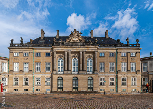 Copenhagen, Denmark - September 13, 2010: Closeup of brown stone and black roof Christian VIII Palace on Amalienborg under bue cloudscape. Red guard poles add color