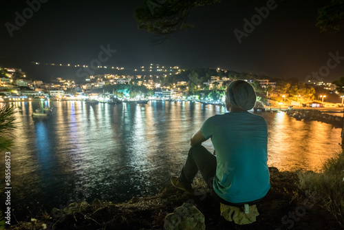 Mann mit Strickm  tze genie  t Ausblick auf n  chtlich beleuchtetes Fischerdorf am Mittelmeer