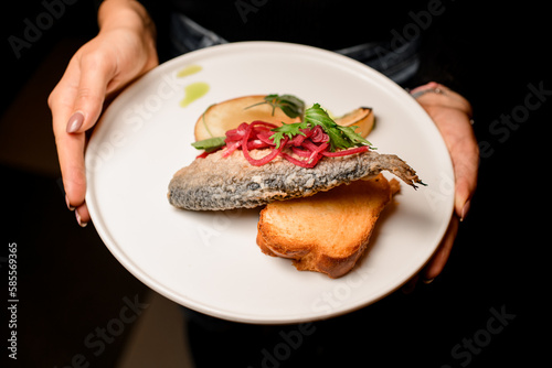view on plate with delicious fried fish garnished with onion and lemon and toast in female hands